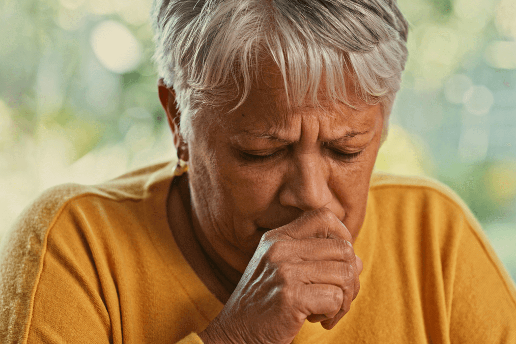 Older woman in a yellow top coughing