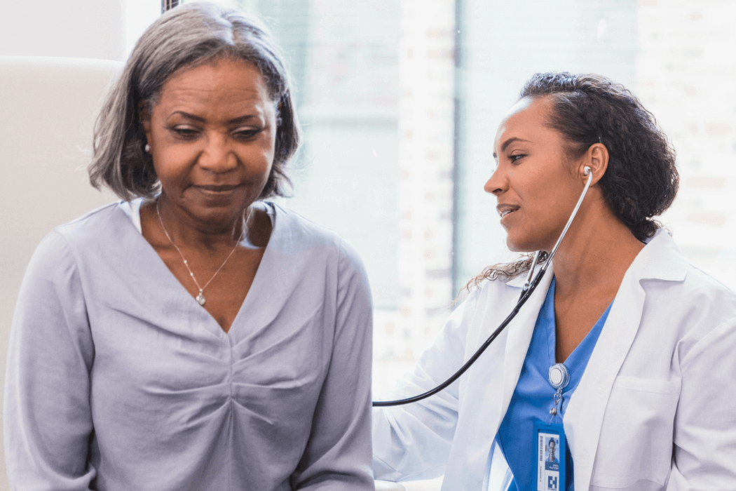 Young woman doctor checking the breathing of an older woman patient.