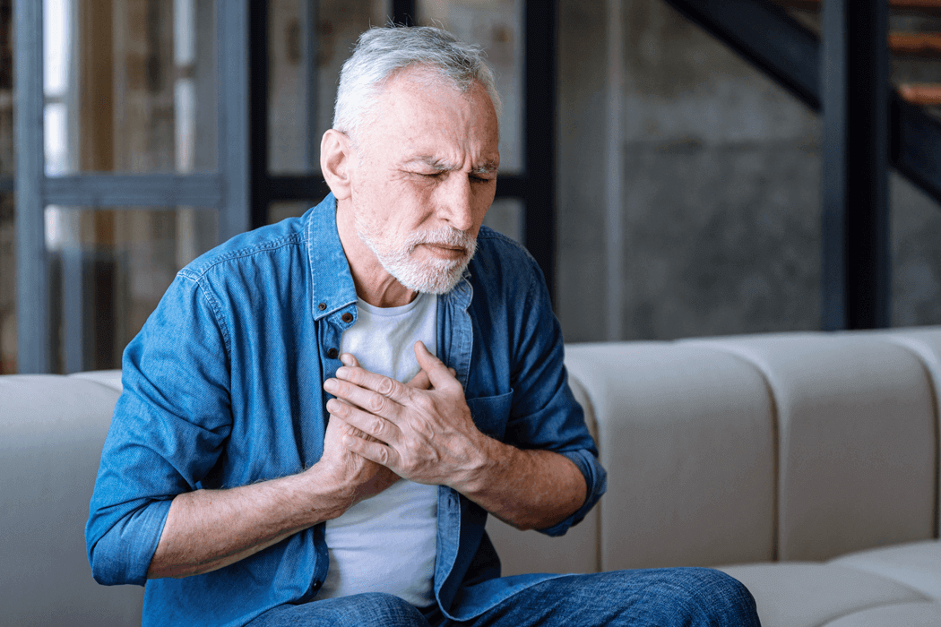 Older man sitting on a couch and holding his chest in discomfort