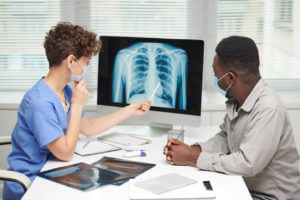 pulmonologist demonstrating x-ray shot to patient on computer screen and explaining something to him