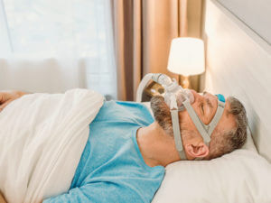 Middle-aged man sleeping in bed while wearing a CPAP mask for sleep apnea treatment, demonstrating proper use of continuous positive airway pressure therapy