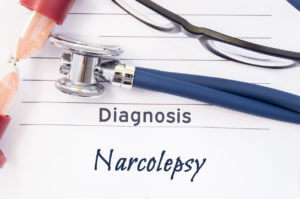 Image of Narcolepsy Diagnosis. The psychiatric diagnosis of narcolepsy is written on a piece of paper, on which a stethoscope and an hourglass lay.