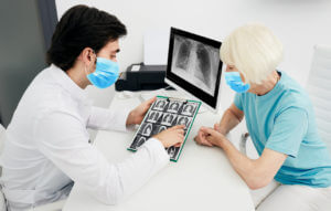 A pulmonologist wearing a protective mask shows a senior patient with pulmonary fibrosis a CT scan of her lungs.